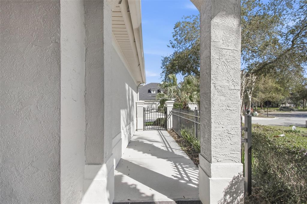 A concrete walkway leads past a stucco wall toward a metal gate and fence — 3 RIVER PARK DRIVE N, PALM COAST, FL