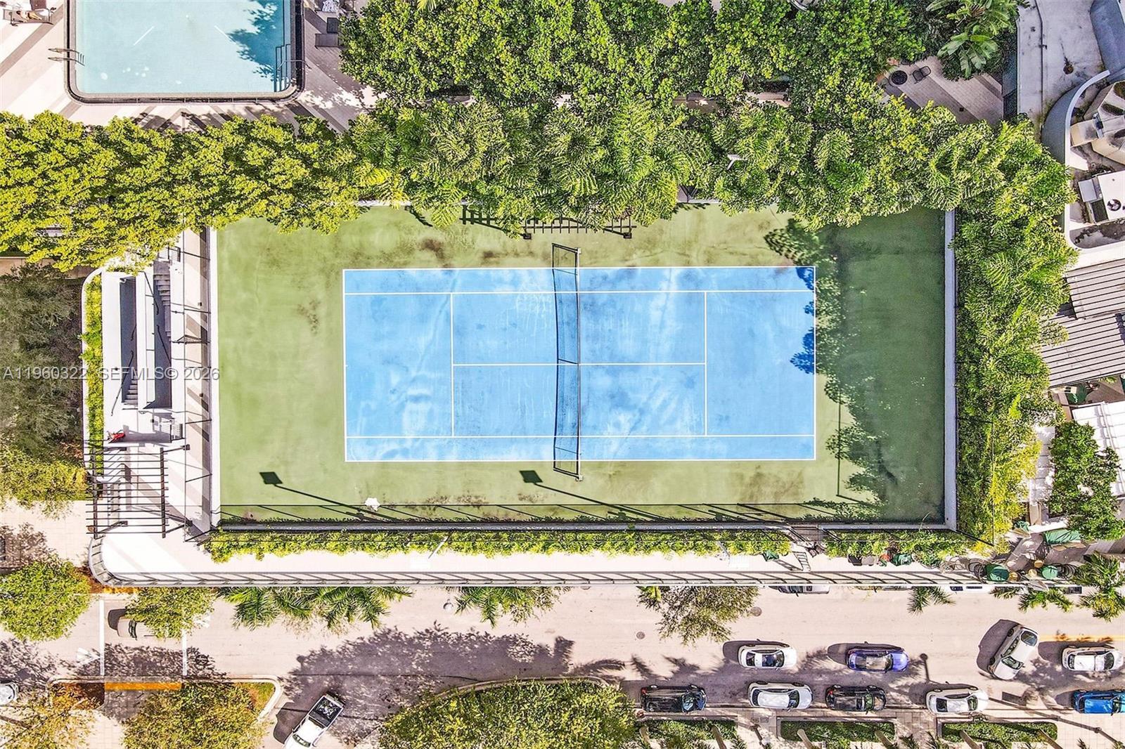 An aerial view of a blue tennis court surrounded by trees and a parking area — 121 NE 34th St # 2305, Miami FL 33137, MIAMI, FL