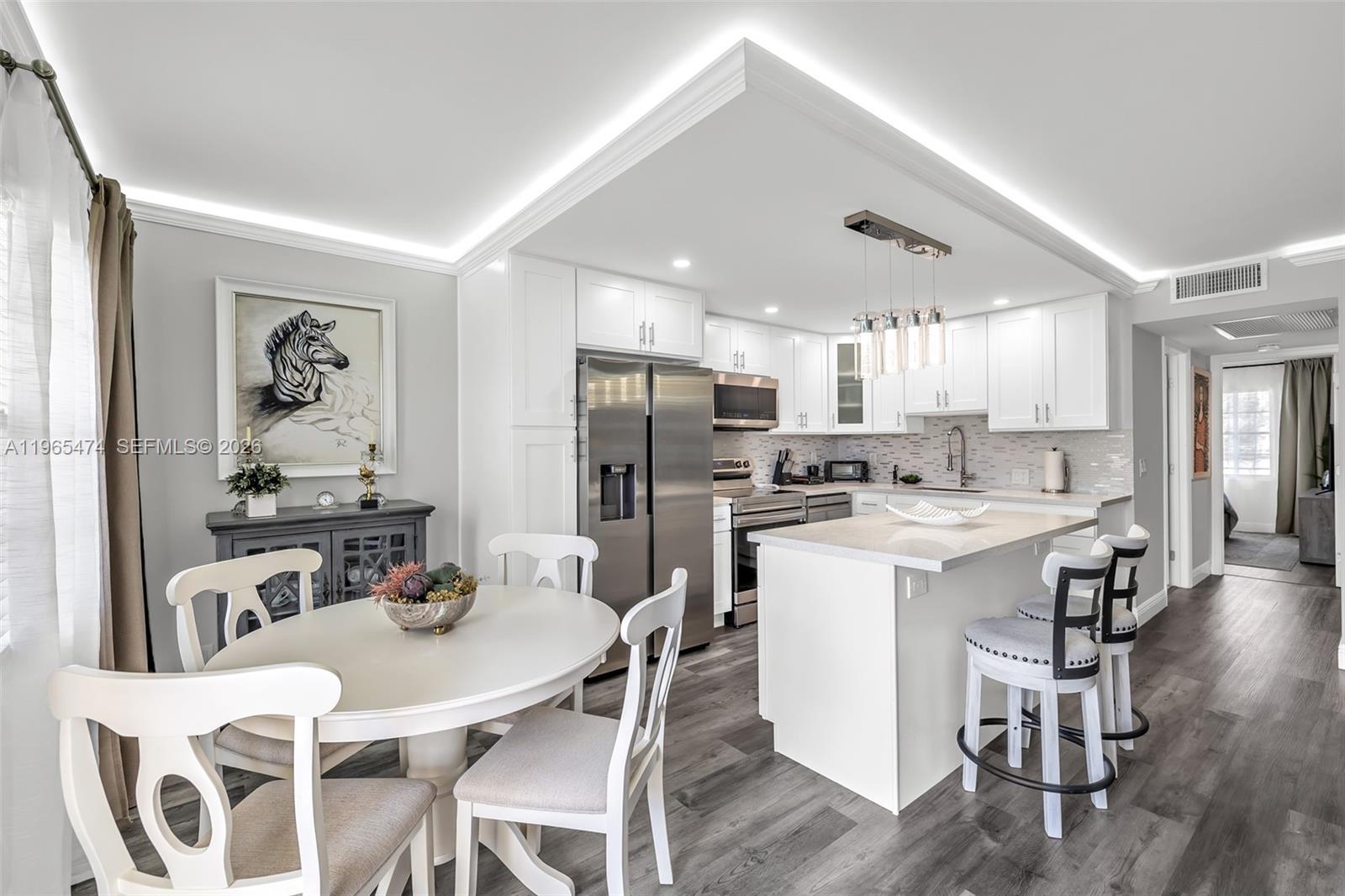 A modern kitchen features white cabinetry, stainless steel appliances, a center island, and dining area — 152 Dorset D # 152, Boca Raton FL 33434, BOCA RATON, FL