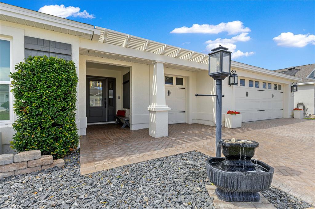 The exterior of a house features a paved driveway, a fountain, and a covered entryway — 1132 MAYNARD PATH, THE VILLAGES, FL