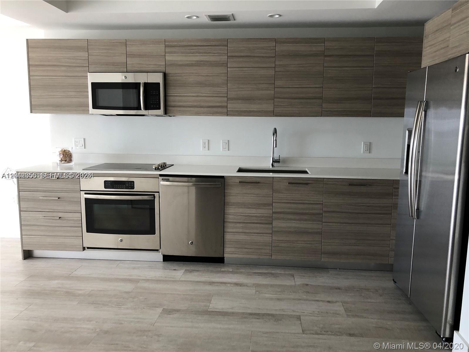 A modern kitchen features wood-grain cabinets, stainless steel appliances, and white countertops — 121 NE 34th St # 2306A, Miami FL 33137, MIAMI, FL