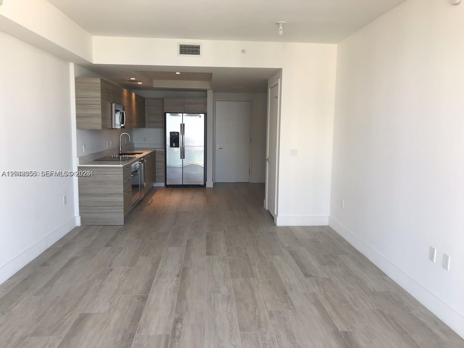 An open-concept kitchen with wood-grain cabinets and stainless steel appliances sits beside a living area — 121 NE 34th St # 2306A, Miami FL 33137, MIAMI, FL