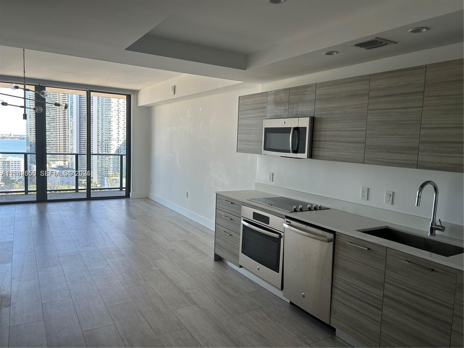 A modern kitchen features wood-grain cabinets, stainless steel appliances, and a view of city skyscrapers — 121 NE 34th St # 2306A, Miami FL 33137, MIAMI, FL