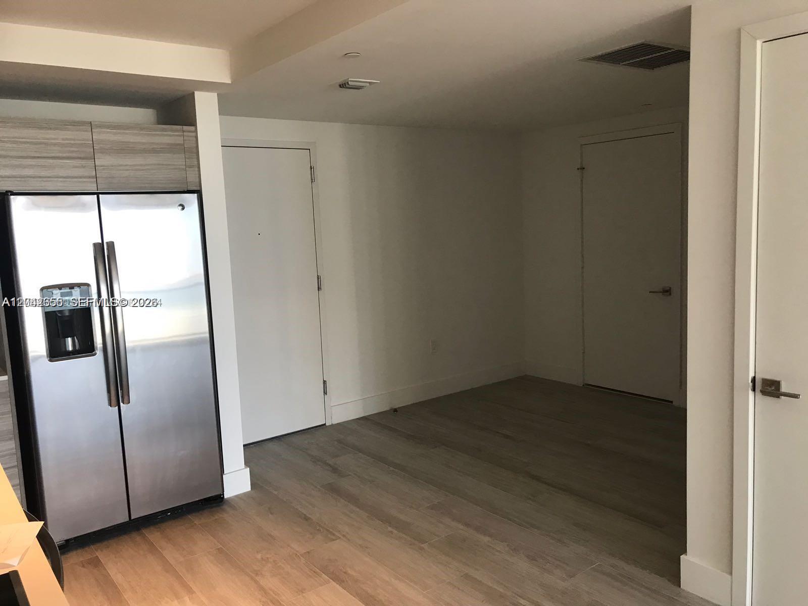 A stainless steel refrigerator stands next to a doorway in a room with wood-look flooring — 121 NE 34th St # 2306A, Miami FL 33137, MIAMI, FL