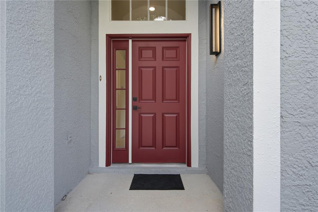 A red front door with a side window light is set in a gray stucco entryway — 6003 CHELLAS COURT, LUTZ, FL