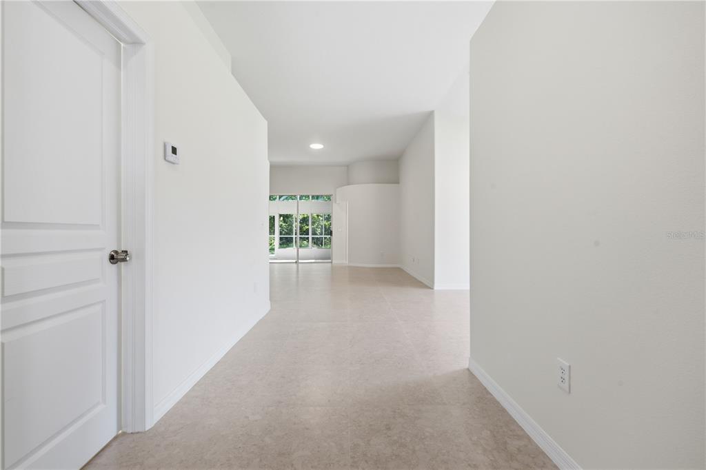 A bright hallway with light-colored tile flooring leads toward a living area with sliding glass doors — 6003 CHELLAS COURT, LUTZ, FL