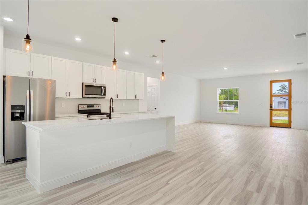 A modern kitchen with white cabinets and a large island opens into a spacious living area — 417 MARION OAKS LANE, OCALA, FL