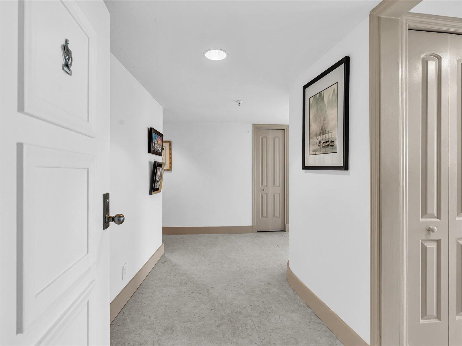 A hallway with white walls, light gray flooring, and beige trim leads to a closed door — 3360 S Ocean Boulevard # 2a, Palm Beach FL 33480, PALM BEACH, FL
