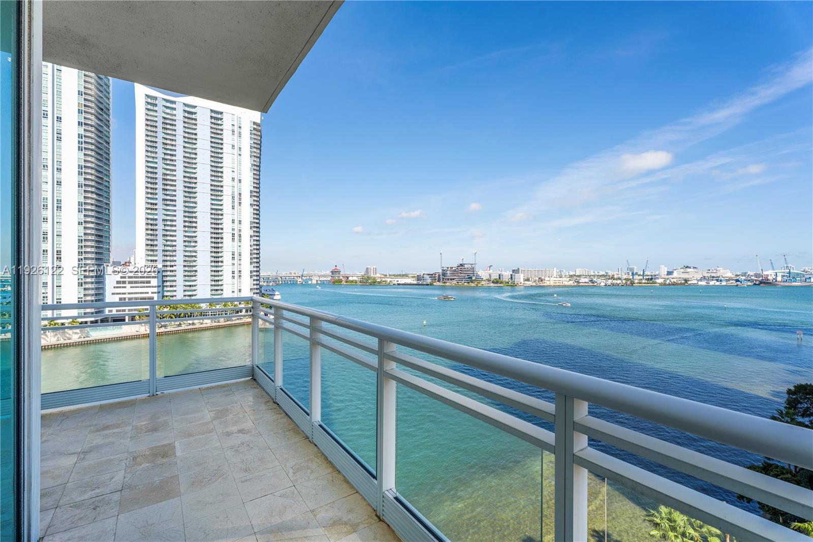 A balcony with a glass railing overlooks a bay with high-rise buildings in the distance — 900 Brickell Key Blvd # 803, Miami FL 33131, MIAMI, FL
