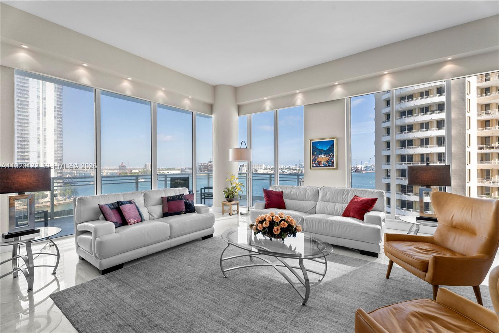 A bright living room features two white sofas, leather chairs, and floor-to-ceiling windows overlooking water — 900 Brickell Key Blvd # 803, Miami FL 33131, MIAMI, FL