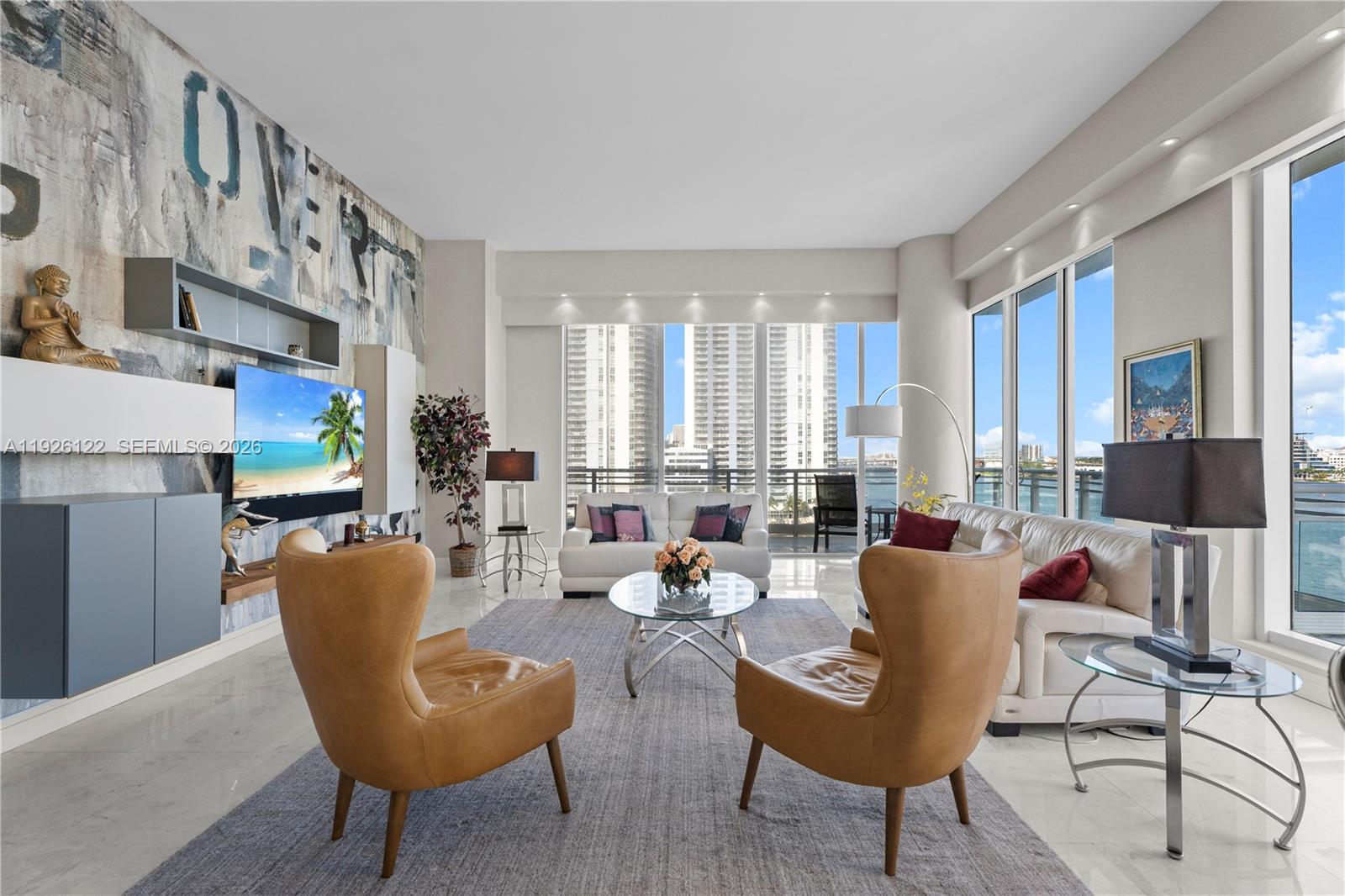 A modern living room features a large mural, leather armchairs, and floor-to-ceiling windows overlooking water — 900 Brickell Key Blvd # 803, Miami FL 33131, MIAMI, FL