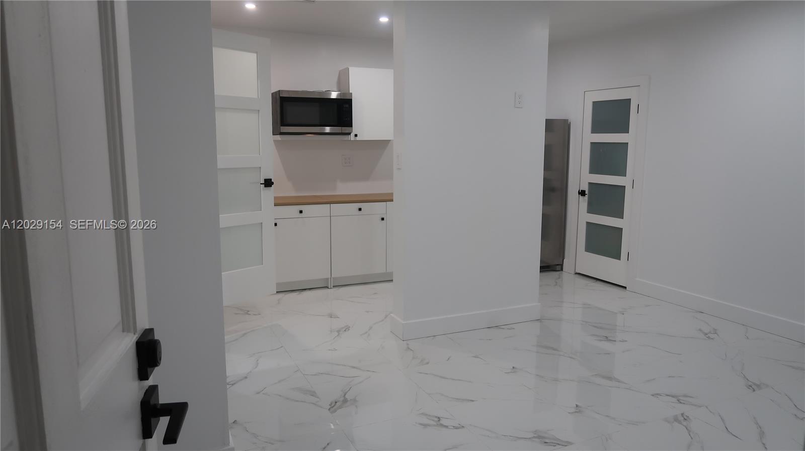 A kitchen area features white cabinets, a microwave, and white marble-patterned tile flooring — 8220 NW 199th St # 1, Hialeah FL 33015, HIALEAH, FL