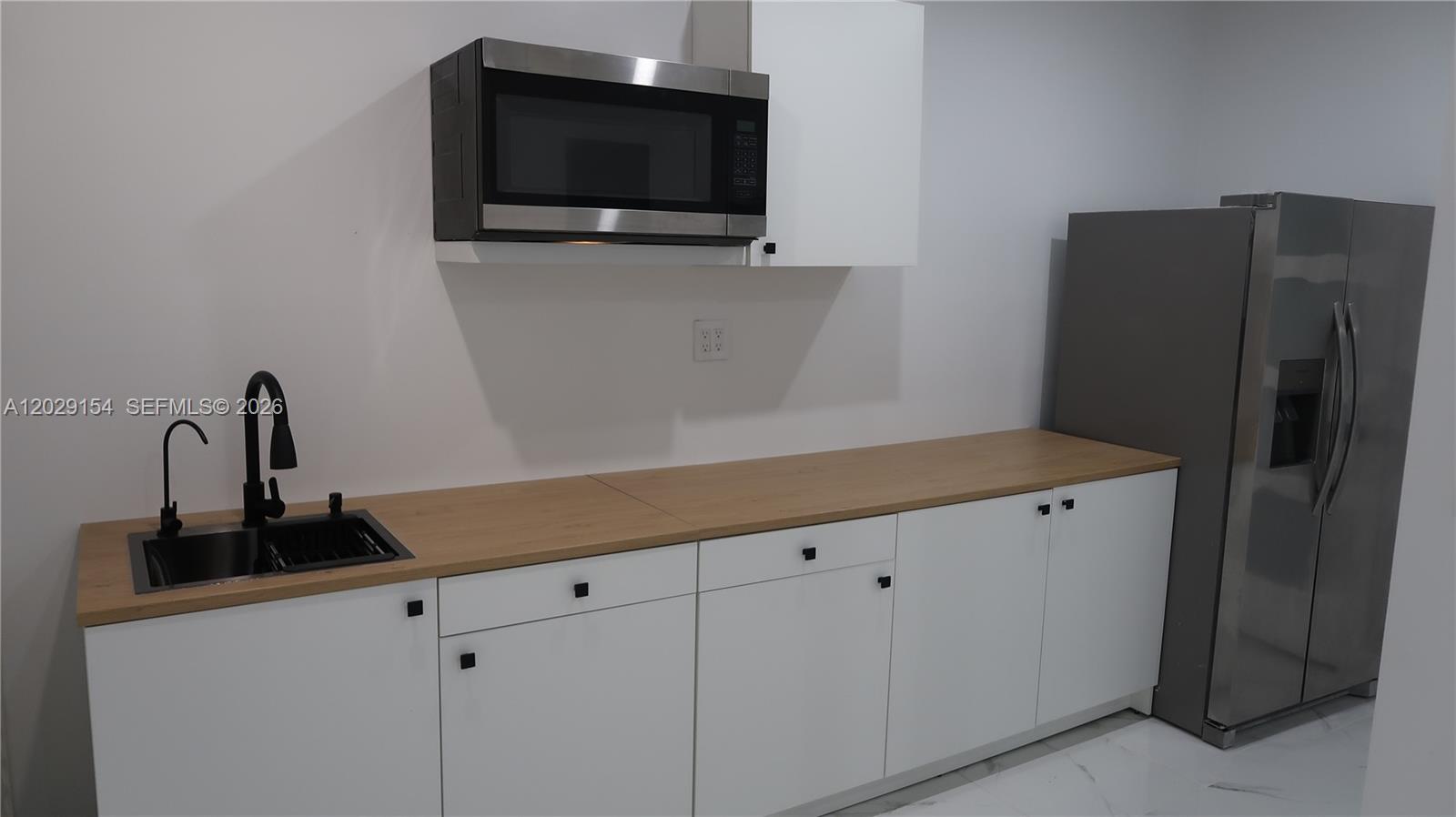 A kitchen features white cabinets, a wood-look countertop, a black sink, and stainless steel appliances — 8220 NW 199th St # 1, Hialeah FL 33015, HIALEAH, FL