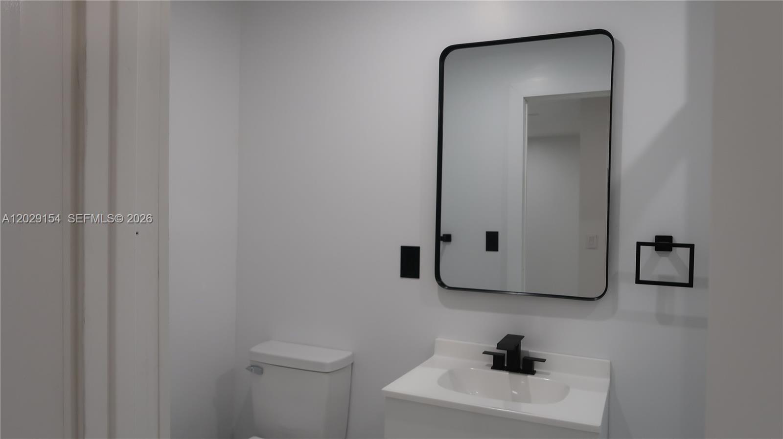 A modern bathroom features a white vanity, a black-framed mirror, and a toilet — 8220 NW 199th St # 1, Hialeah FL 33015, HIALEAH, FL