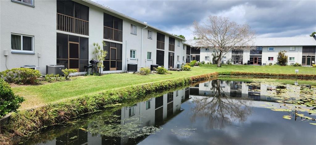 A two-story apartment building sits beside a pond with lily pads and grassy landscaping — 11201 122ND AVENUE UNIT L-232, LARGO, FL