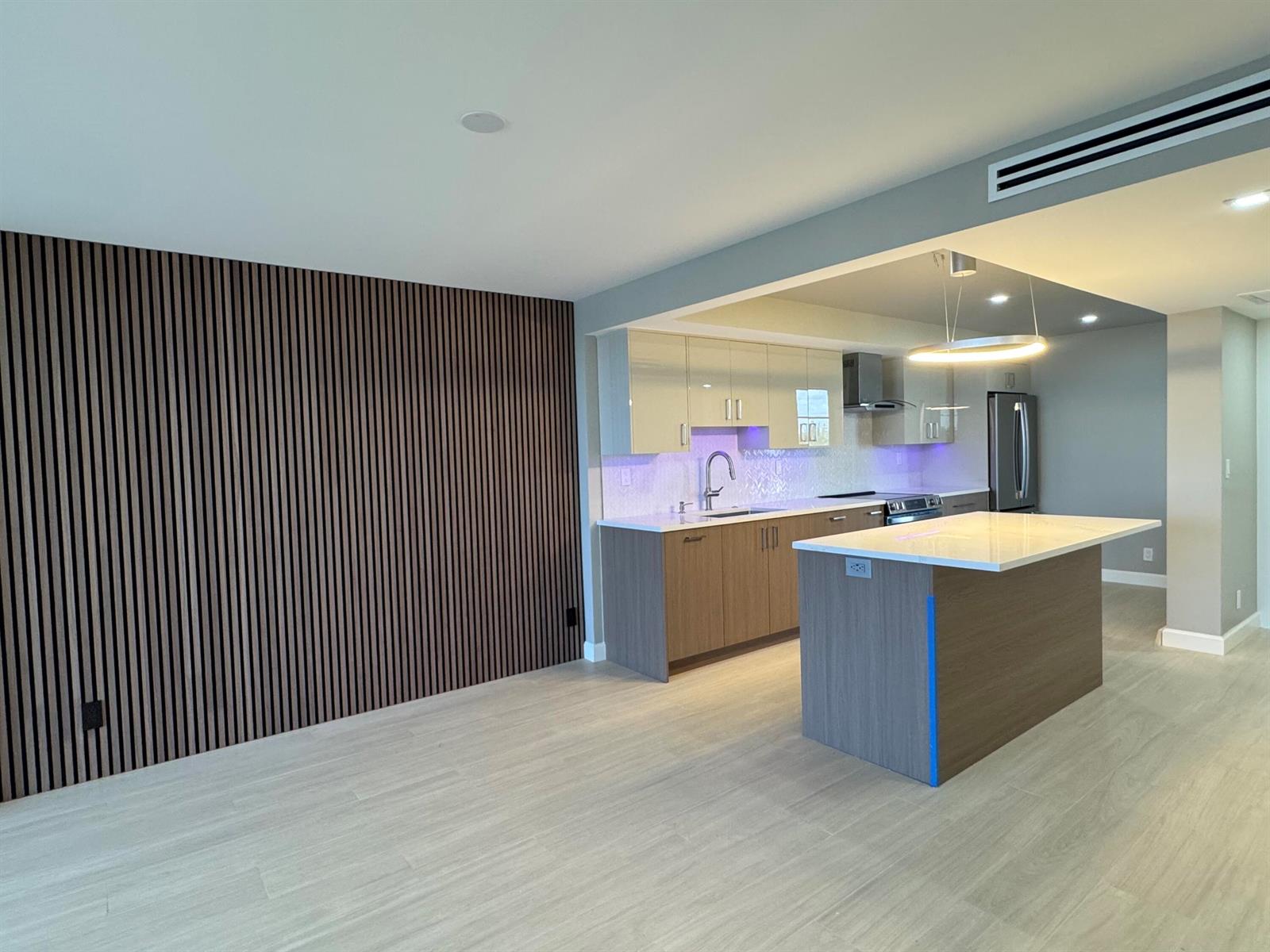 A modern kitchen features wood-slat wall paneling, a central island, and light-colored cabinetry — 12 Royal Palm Way # 6030, Boca Raton FL 33432, BOCA RATON, FL