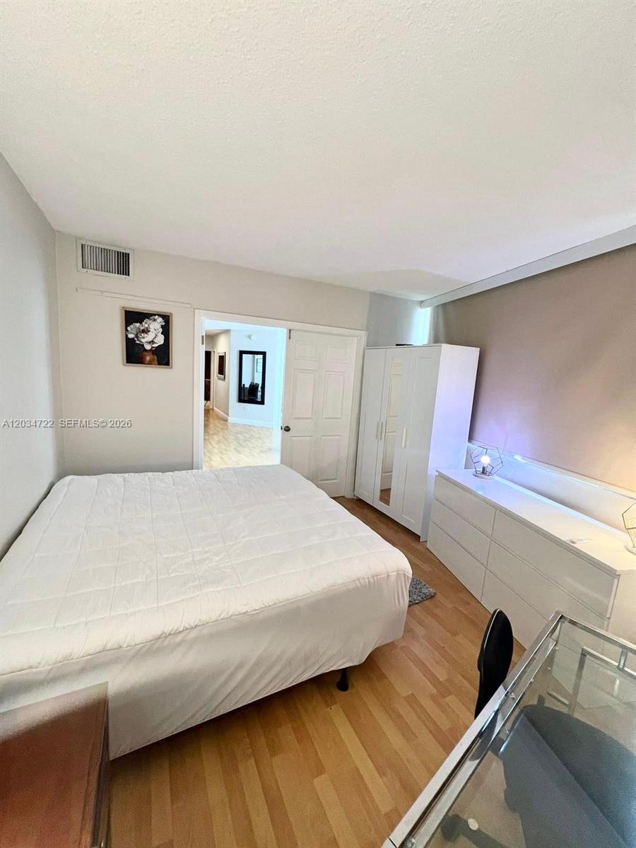A bedroom features a white bed, a white wardrobe, a dresser, and wood flooring — 905 Brickell Bay Dr # 1422, Miami FL 33131, MIAMI, FL