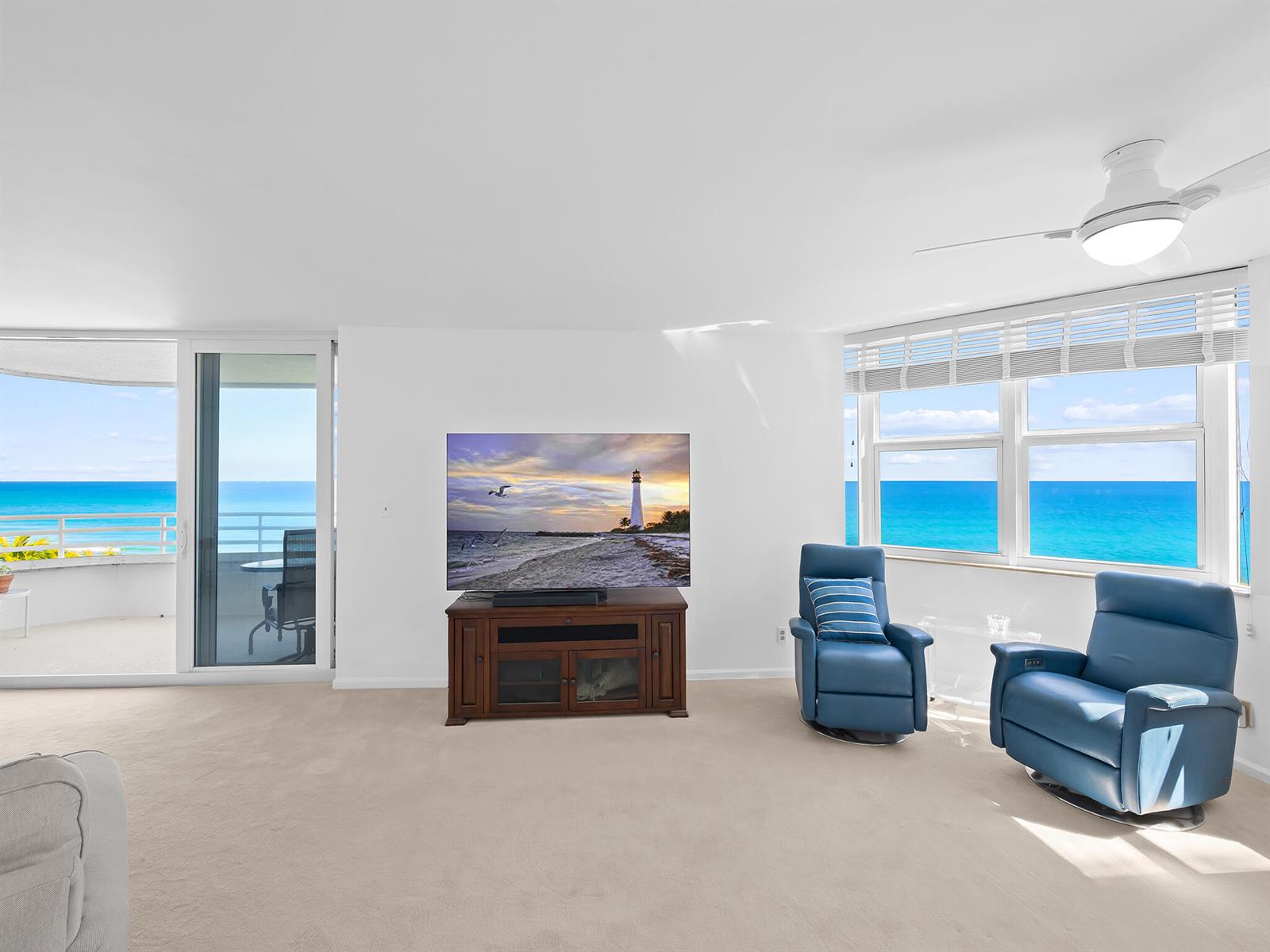 A living room features a television on a wooden stand, two blue chairs, and ocean views — 3407 S Ocean Boulevard # 7a, Highland Beach FL 33487, HIGHLAND BEACH, FL
