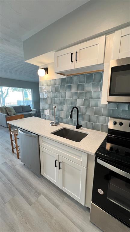 A kitchen features white cabinets, a blue tiled backsplash, a stainless steel sink, and appliances — 974 TENNESSEE LANE, SARASOTA, FL