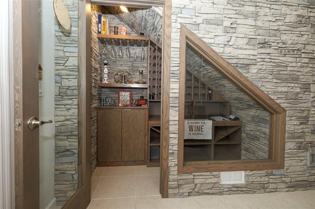 A stone-walled wine cellar features custom wooden shelving, glass-fronted storage, and a glass viewing window — 3980 LIGHTNING COURT, SANFORD, FL