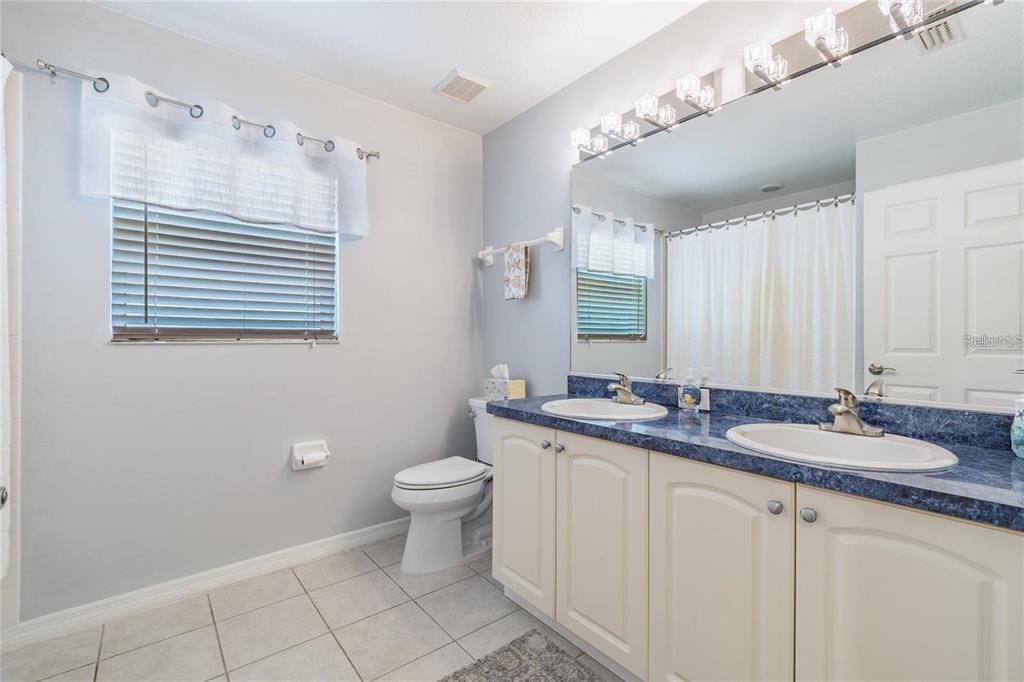 A bathroom features a double vanity with blue countertops, a toilet, and a shower-tub combo — 9501 27TH AVENUE E, PALMETTO, FL