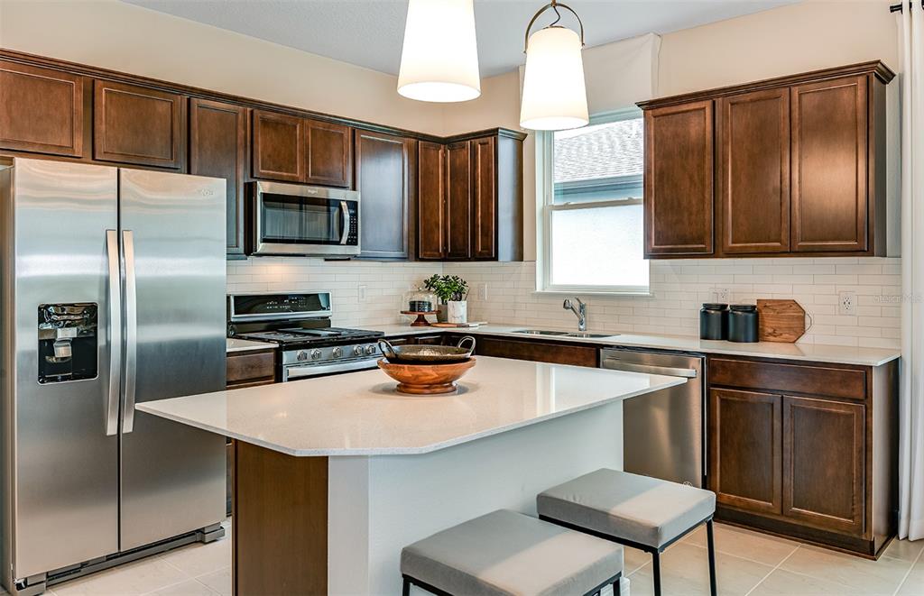 A kitchen with dark wood cabinets, stainless steel appliances, a white island, and pendant lighting — 12514 ADOBE STREET, PARRISH, FL