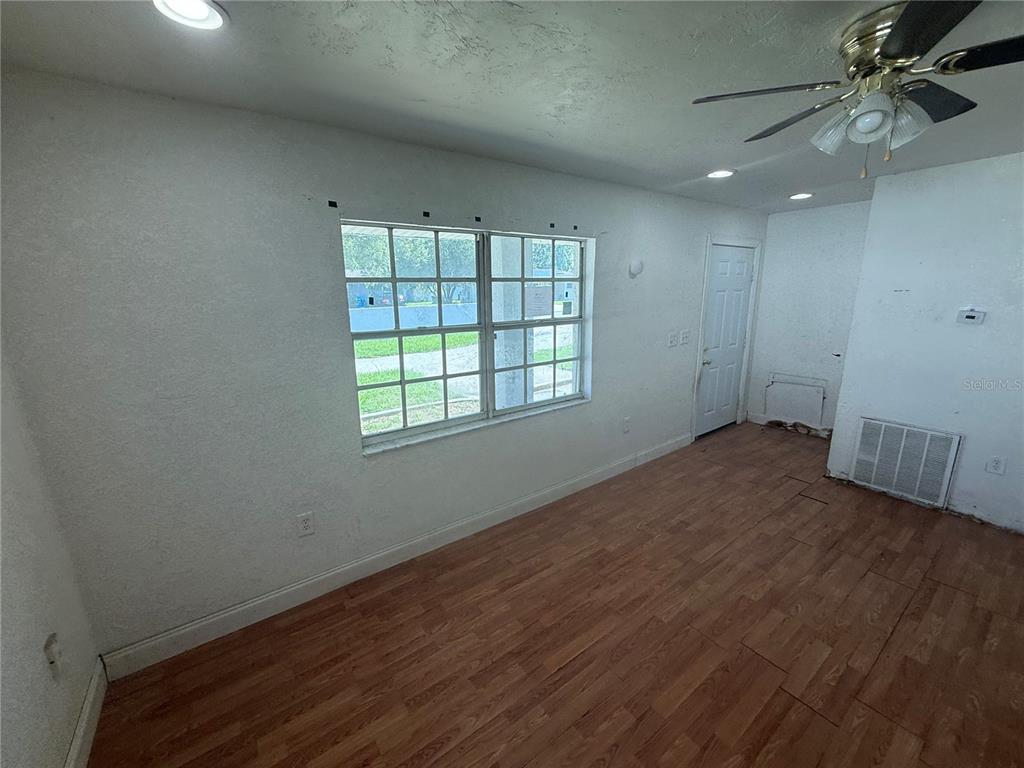 An empty room features wood-look flooring, a ceiling fan, a window, and a white door — 2442 LILLY STREET, LAKE WALES, FL