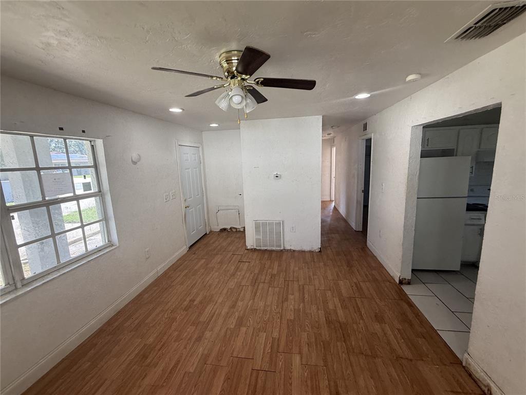 An interior view shows a room with wood-look flooring, a ceiling fan, and a kitchen doorway — 2442 LILLY STREET, LAKE WALES, FL