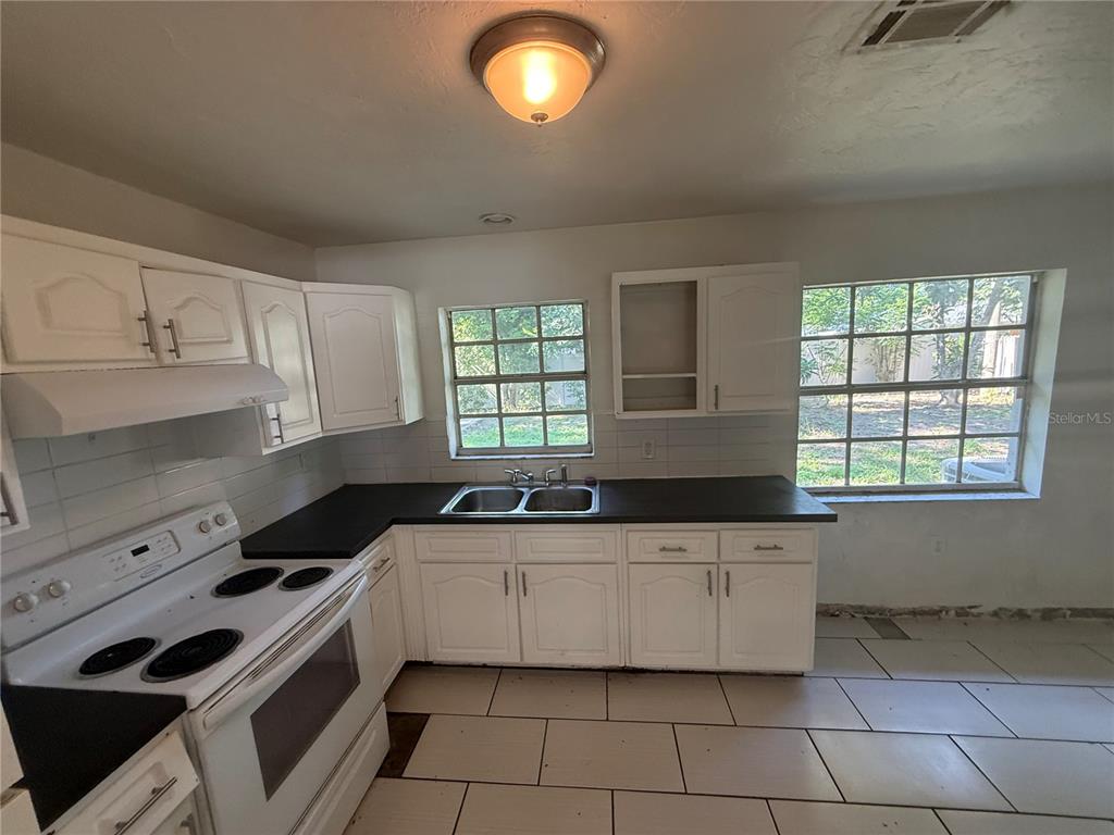A kitchen features white cabinets, black countertops, a white stove, and two windows — 2442 LILLY STREET, LAKE WALES, FL