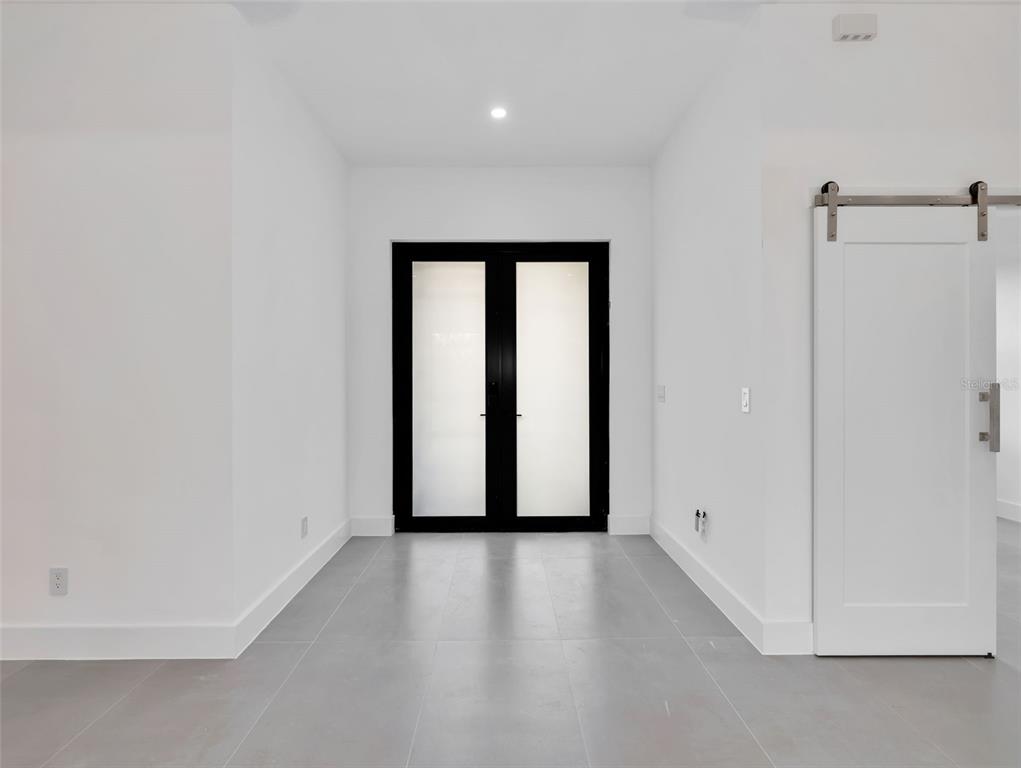 A minimalist hallway features white walls, gray tile flooring, black-framed glass doors, and a sliding door — 11042 CARNEGIE AVENUE, ENGLEWOOD, FL
