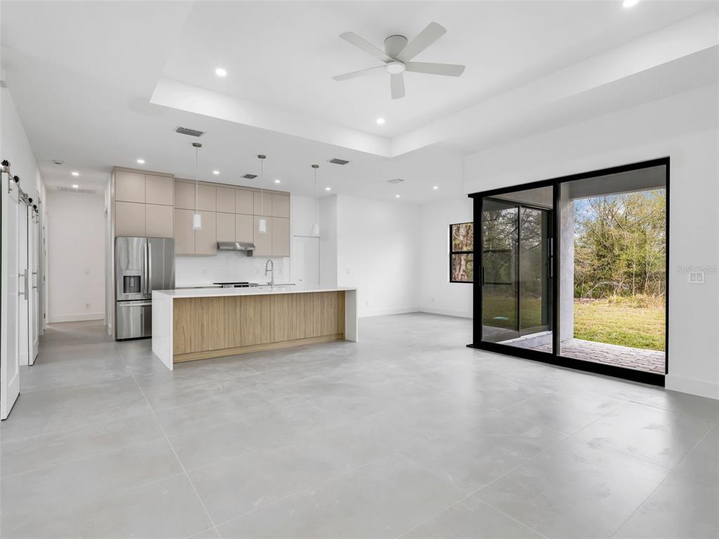 A modern kitchen and living area with light wood cabinetry, a white island, and sliding doors — 11042 CARNEGIE AVENUE, ENGLEWOOD, FL