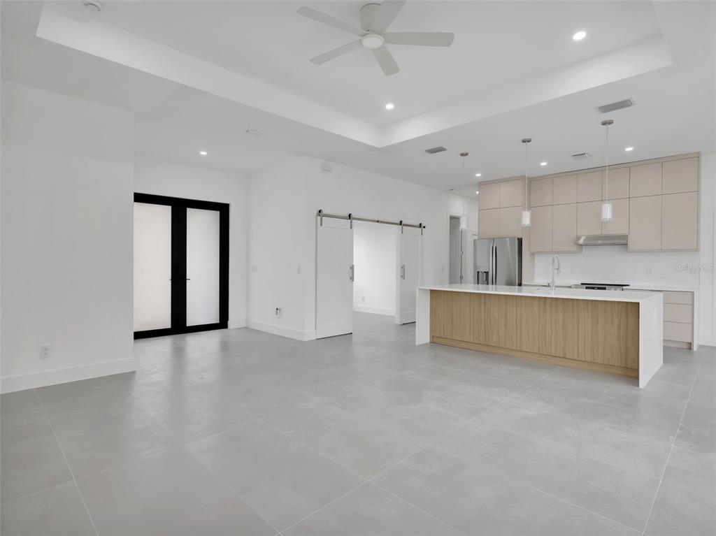 A modern open-concept kitchen and living area featuring light wood cabinetry, white countertops, and tile flooring — 11042 CARNEGIE AVENUE, ENGLEWOOD, FL