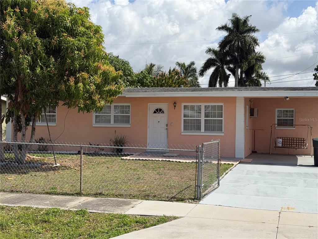 A single-story peach-colored house features a white front door, a carport, and a chain-link fence — 32 ROANOKE DRIVE UNIT 0, FORT MYERS, FL