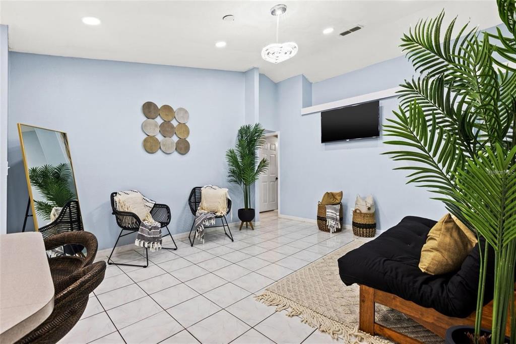 A living room with light blue walls, tile flooring, a black futon, and two chairs — 5102 N MACDILL AVENUE, TAMPA, FL