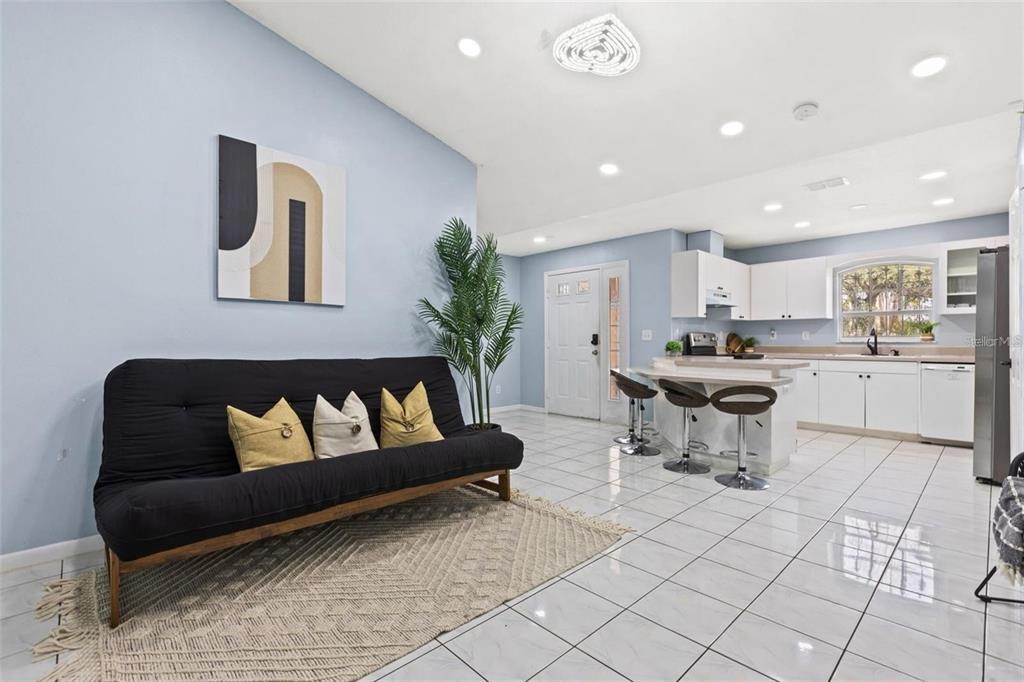 An open-concept living room and kitchen with white cabinets, tile flooring, and a black futon — 5102 N MACDILL AVENUE, TAMPA, FL