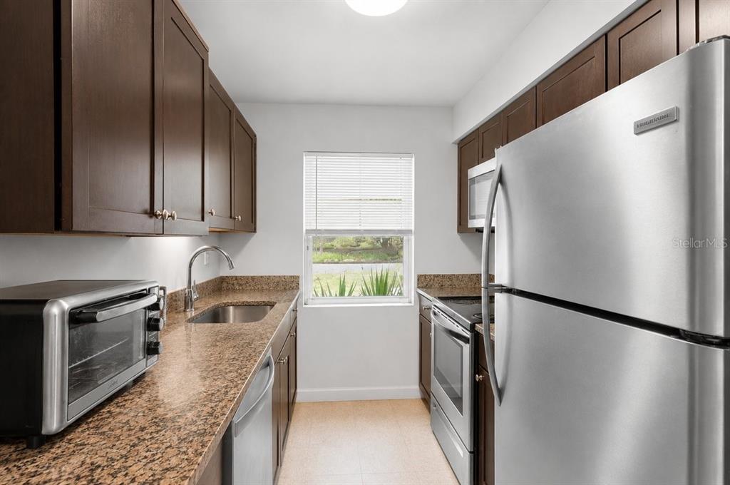 A galley kitchen features dark wood cabinets, granite countertops, and stainless steel appliances — 1812 SW 70TH TERRACE, GAINESVILLE, FL
