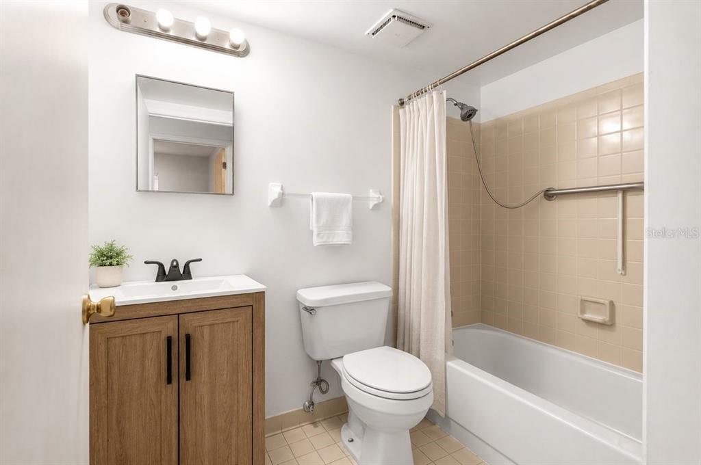 A bathroom features a wood vanity, a toilet, and a shower-tub combo with beige tiles — 1812 SW 70TH TERRACE, GAINESVILLE, FL