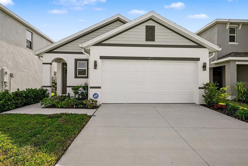 A single-story suburban house with a two-car garage and a concrete driveway at sunset — 6298 WANDERING WILLOW DRIVE, WESLEY CHAPEL, FL