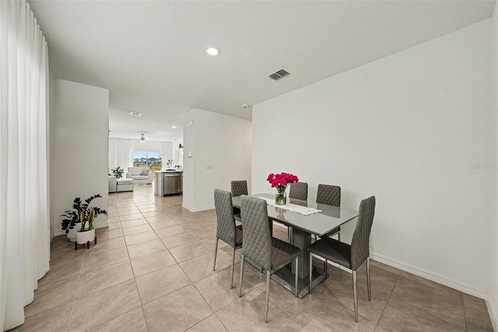 A dining area with a grey table and chairs sits on tiled floors near a kitchen — 6298 WANDERING WILLOW DRIVE, WESLEY CHAPEL, FL