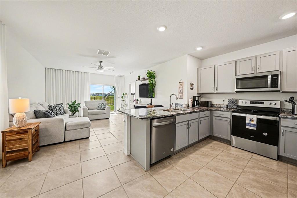 An open-concept kitchen and living area features light gray cabinets, tile flooring, and sliding doors — 6298 WANDERING WILLOW DRIVE, WESLEY CHAPEL, FL
