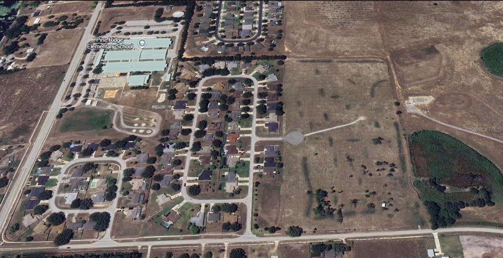 This aerial view shows a residential neighborhood adjacent to Pine Ridge Elementary School and undeveloped land — LOT 3 MERCADO COURT, CLERMONT, FL