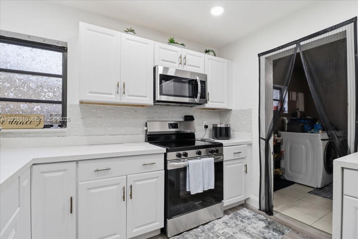 A white kitchen features stainless steel appliances, white cabinetry, and a tiled backsplash — 7551 Polk St, Hollywood FL 33024, HOLLYWOOD, FL