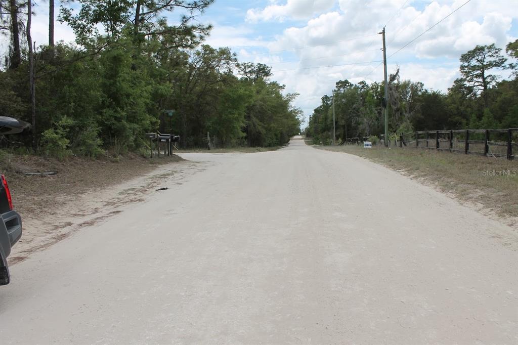 A dirt road stretches into a wooded area with a wooden fence on the right — NE 56TH STREET, BRONSON, FL