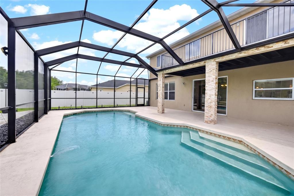 A swimming pool with steps sits inside a screened-in patio next to a two-story house — 11384 WALDEN LOOP, PARRISH, FL