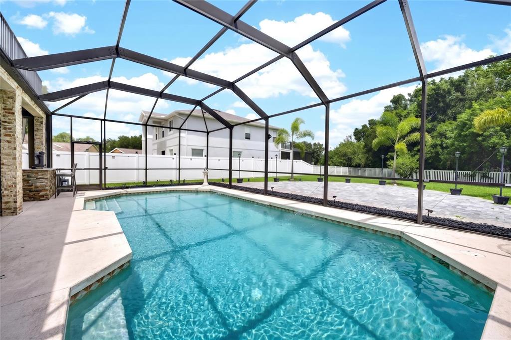 A swimming pool sits inside a screened-in lanai with a paved patio and stone accents — 11384 WALDEN LOOP, PARRISH, FL