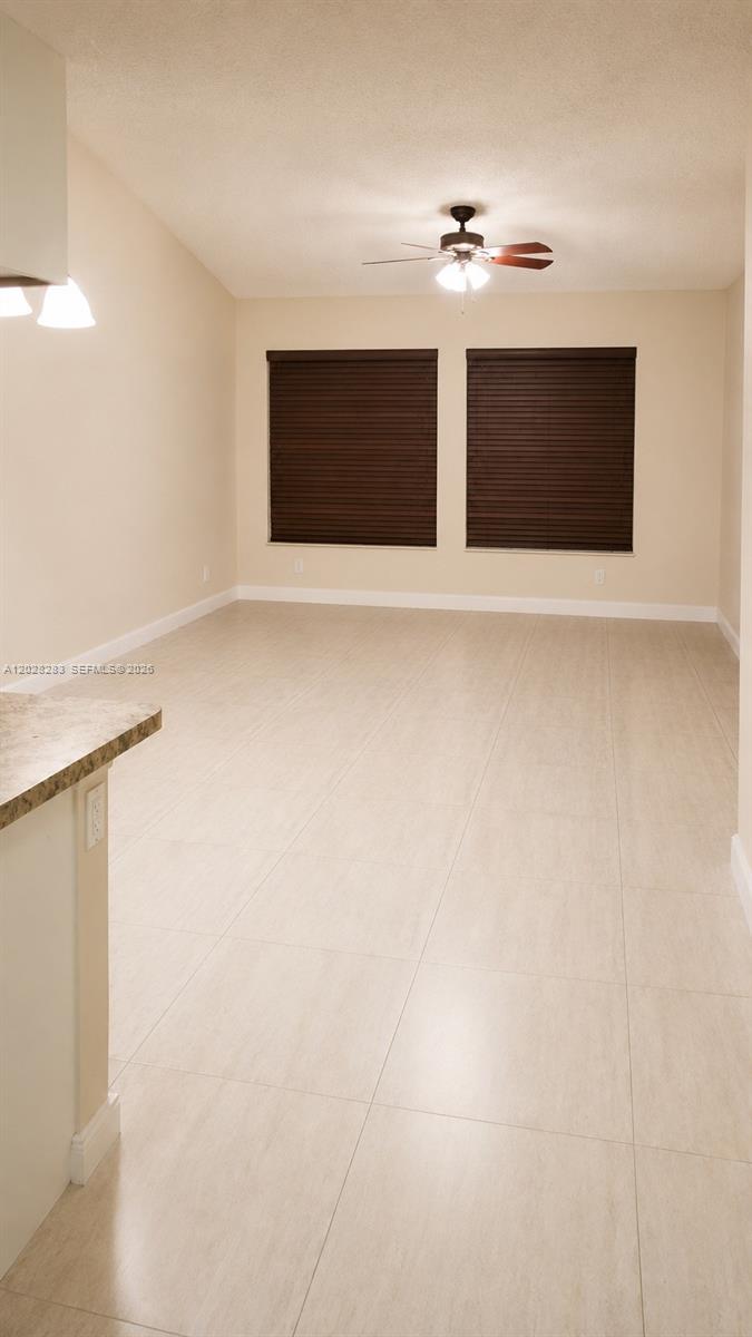An empty room features light-colored tile flooring, beige walls, and a ceiling fan — 6292 La Costa Dr # M, Boca Raton FL 33433, BOCA RATON, FL