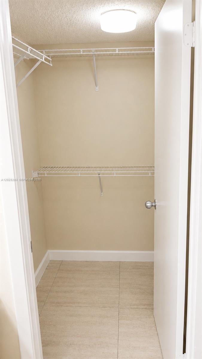 A walk-in closet features white wire shelving, beige walls, and light-colored tile flooring — 6292 La Costa Dr # M, Boca Raton FL 33433, BOCA RATON, FL