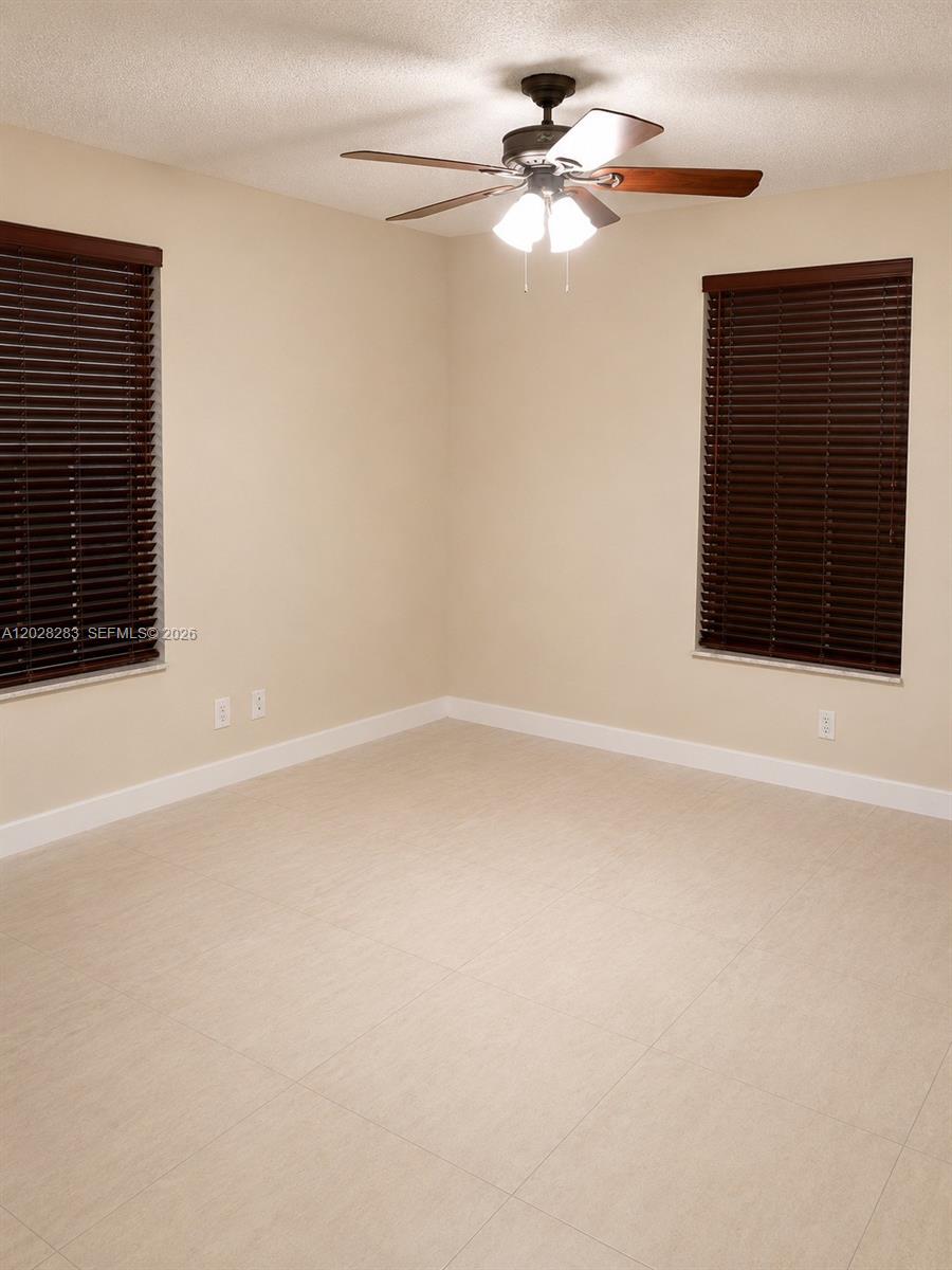 An empty room features beige walls, tile flooring, two windows with dark blinds, and a ceiling fan — 6292 La Costa Dr # M, Boca Raton FL 33433, BOCA RATON, FL