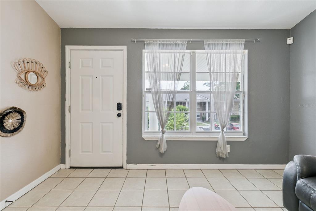 A room with tiled floors, a white front door, and a window with sheer curtains — 145 RESERVE CIRCLE UNIT 205, OVIEDO, FL