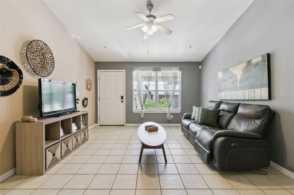 A living room features tile flooring, a leather sofa, a television console, and a ceiling fan — 145 RESERVE CIRCLE UNIT 205, OVIEDO, FL